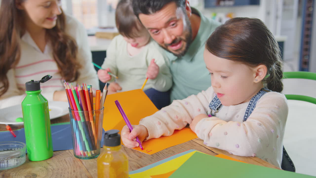 familia con síndrome de down hija sentada alrededor de la mesa en casa haciendo artesanía juntos