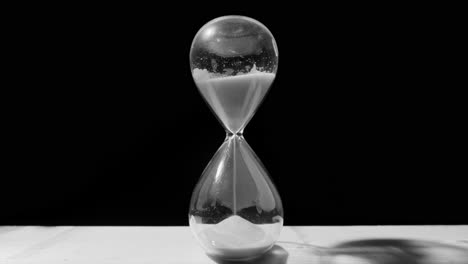 desaturated arcing shot of sand falling in hourglass, time running out concept