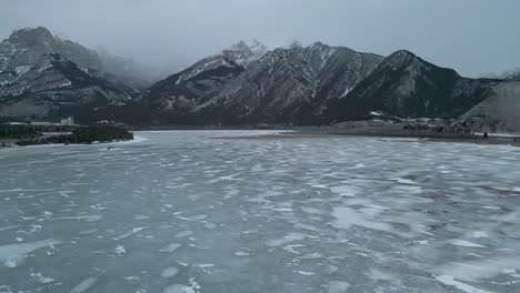 Aerial-view-of-frozen-lake-with-foggy-mountains-in-the-background---Drone-4k