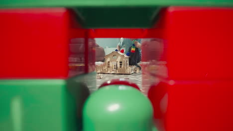 toddler puts colorful plastic blocks on roof of wooden house