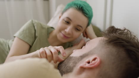 loving caucasian woman touching her boyfriend's face while relaxing on the bed and looking at each other