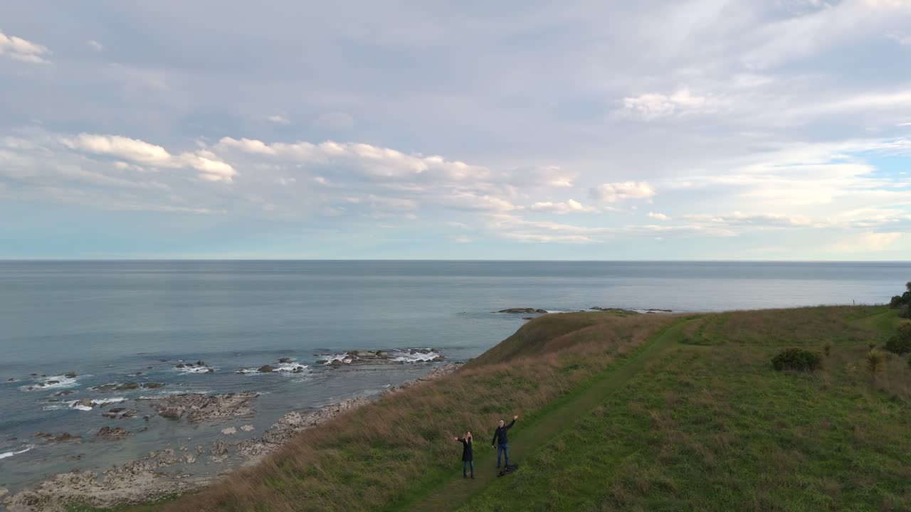 Young couple waving to the drone in Kaikōura coastal pasture