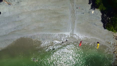 Top-down-aerial-view-of-2-tourists-putting-a-kayak-or-canoe-in-the-ocean-on-tropical-beach