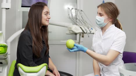 joven dentista ofreciendo manzana verde a un paciente feliz y saludable después de los procedimientos