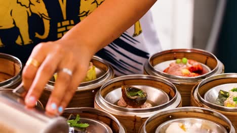 a close-up of a hand pouring sauce over various dim sum baskets in bamboo steamers.