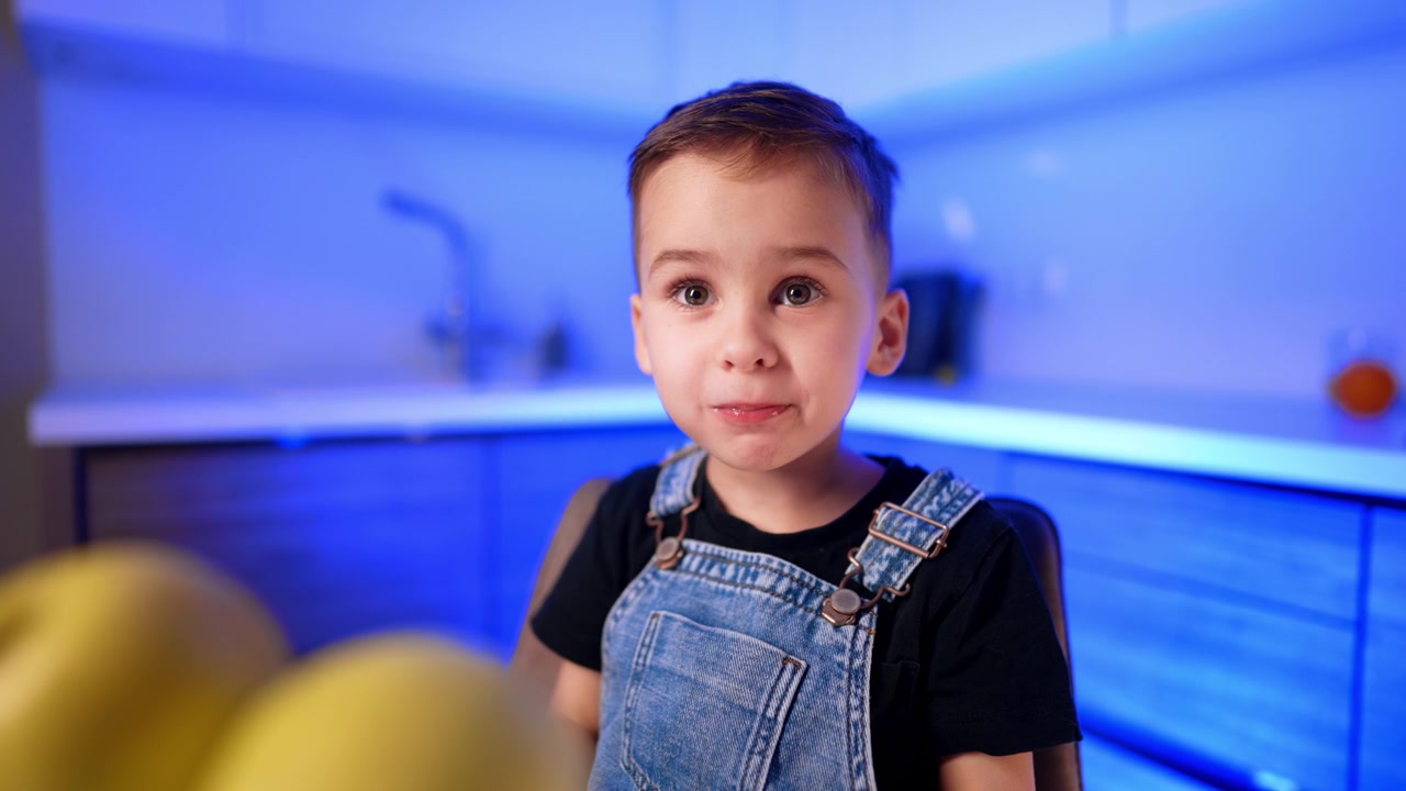 Retrato de cerca de un niño detrás de manzanas amarillas. Mira hacia la cámara mientras las luces frías de la cocina se difuminan en el fondo