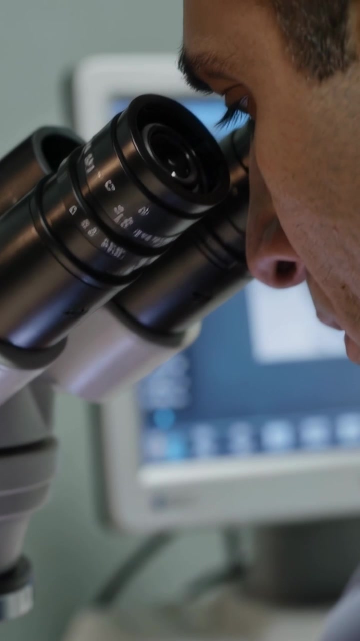 Vertical video: Tech placing slide at lab, tuning stage, peering through scope and inspecting slide