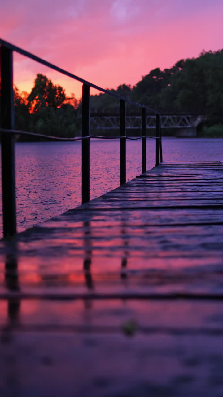 Amazing view of rain falling on the water and footbridge at sunset. Wet wooden bridge over the lake with nobody in the evening in rural place. Vertical video