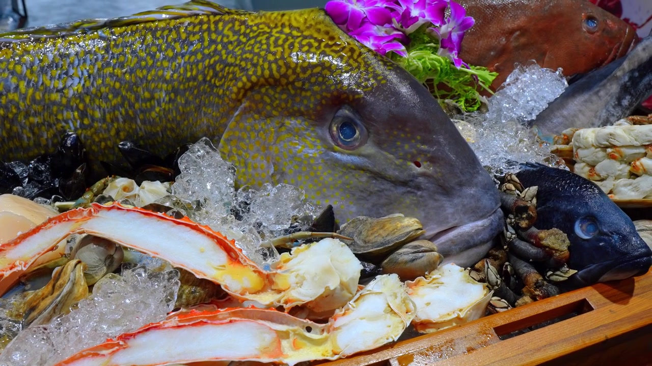 Pesce intero fresco e frutti di mare su ghiaccio in un espositore di cassa di legno. Primo piano di pesce maculato con zampe di granchio, vongole, capesante e ghiaccio tritato.