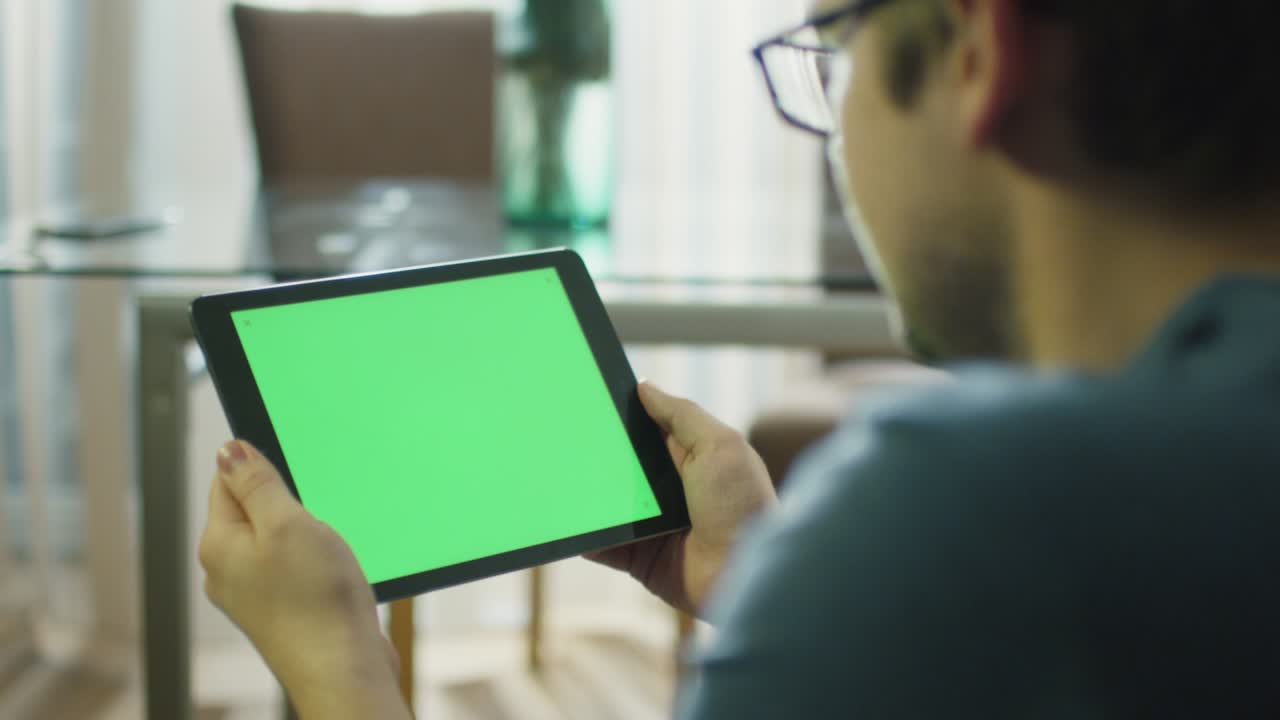 집에서 녹색 화면을 가진 태블릿을 집어 들고 있는 남자가 4k (uhd) 로 빨간 영화관 카메라로 촬영했다.