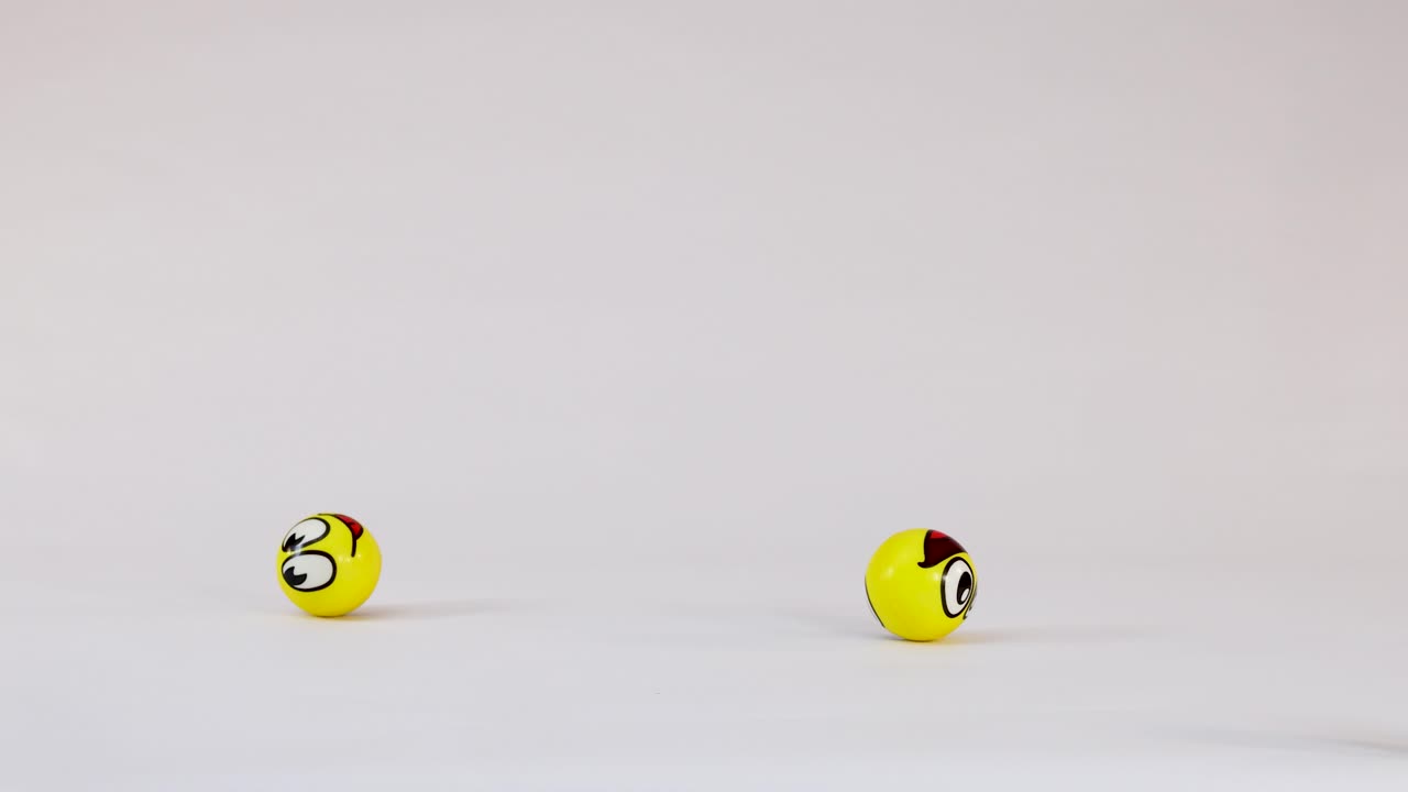 Multiple yellow balls with various emoji faces fall and bounce across a plain white surface