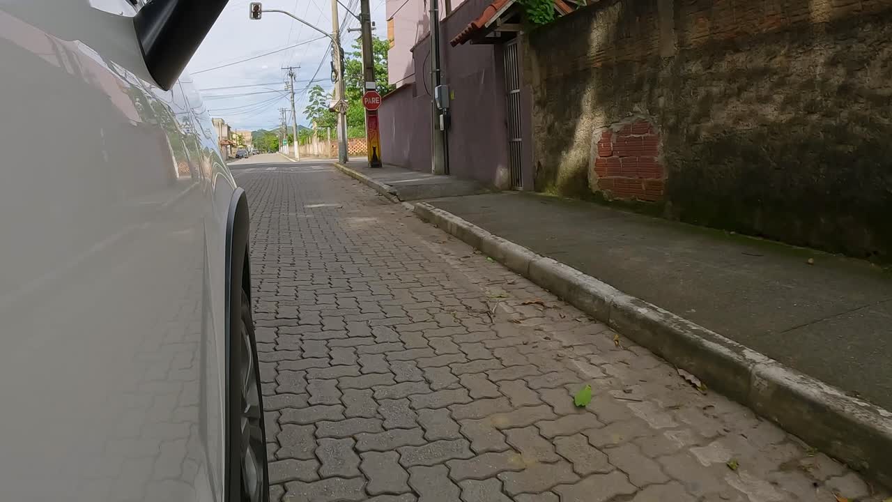 Side point of view shot of a white car driving over a speed bump on a paved suburban street with a wall and houses. Urban driving concept