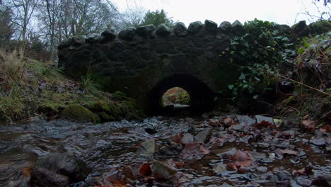 Arroyo-Que-Corre-Por-Debajo-Y-Un-Viejo-Puente-De-Piedra-A-Través-De-Un-Bosque-En-Kinross-Son-Del-Centro-De-Escocia