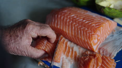 closeup of salmon fillet being sliced with precision for sushi dish in clean prep area, weathered old hands peel meat off of skin
