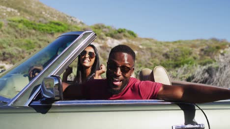 portrait of african american couple waving and having fun while sitting in the convertible car on ro