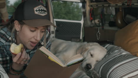 Mujer-Turista-Leyendo-Un-Libro-Mientras-Descansa-En-Una-Furgoneta-Con-Un-Perro