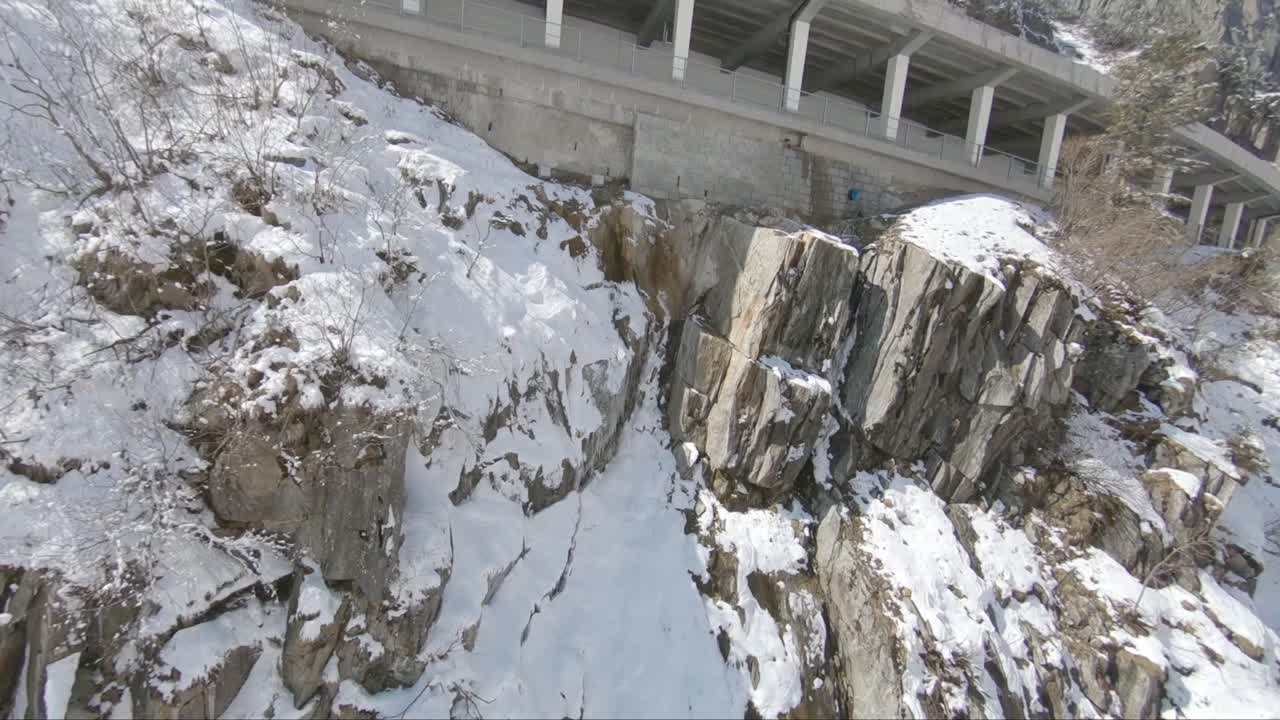 Fast fly by of a mountain pass with a fast car driving inside a tunnel bridge surrounded by snow