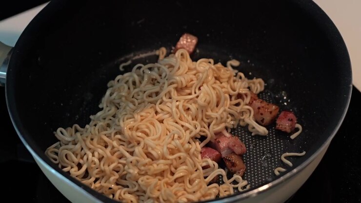 Processo di cottura in padella di noodles saltati con pancetta e carne a cubetti fatta in casa