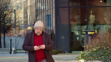 Caucasian-adult-man-walking-street-and-using-mobile-phone,-elegant-style,-front-middle-shot