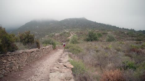 Una-Caminante-Camina-Por-Un-Camino-De-Tierra-Hacia-Una-Montaña-Nublada-Cerca-De-Rosas,-Cataluña,-España