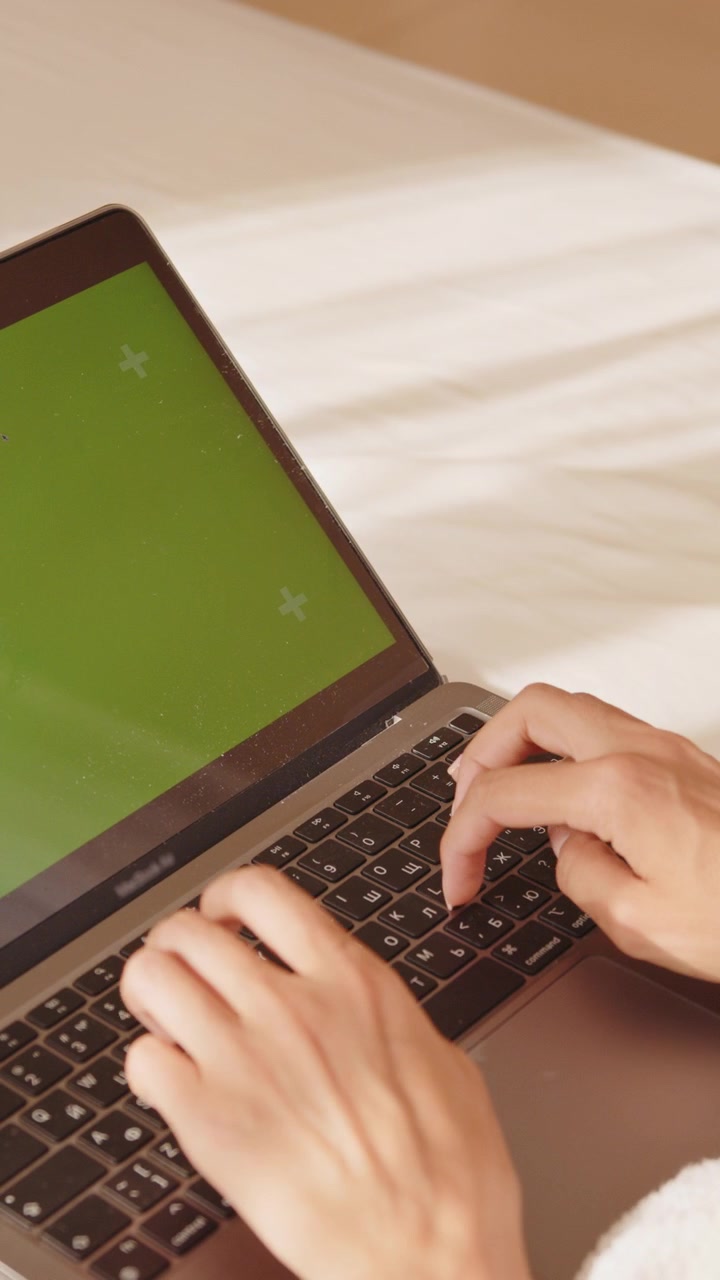 Las manos de una persona tecleando en un portátil con una pantalla verde, perfecto para añadir tu propio contenido, en formato vertical.