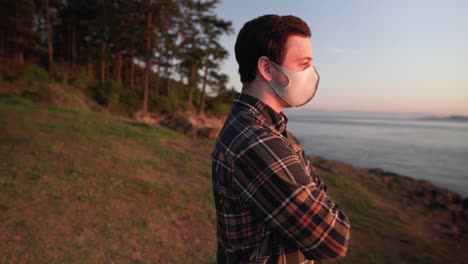 medium slider shot of man wearing face mask watching sunrise over the lake with mountain stretch on the background.