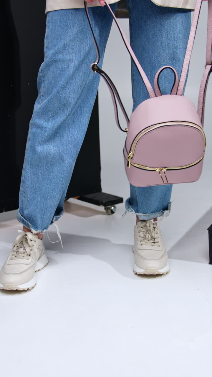 Casual modern lifestyle look. Girl in jeans and white sneakers holding a leather stylish rucksack. Black screen at backdrop. Vertical video