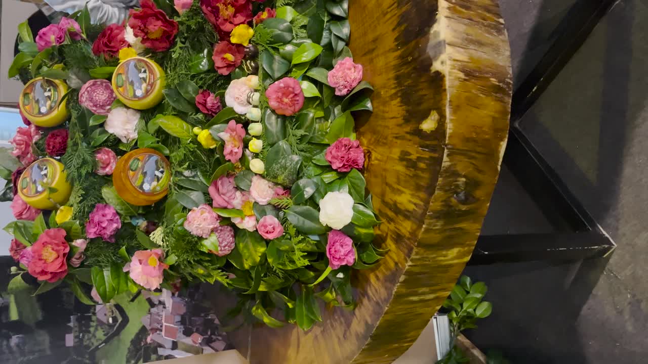 video verticale che mostra una bellissima disposizione floreale con fiori decorativi rosa e verdi vivaci esposti su un tavolo da scrivania in legno rustico, che mescola natura e arte in un'elegante configurazione.