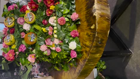 video vertical que muestra un hermoso arreglo floral con vibrantes flores decorativas rosas y verdes exhibidas en una mesa de escritorio de madera rústica, mezclando naturaleza y arte en una configuración elegante.