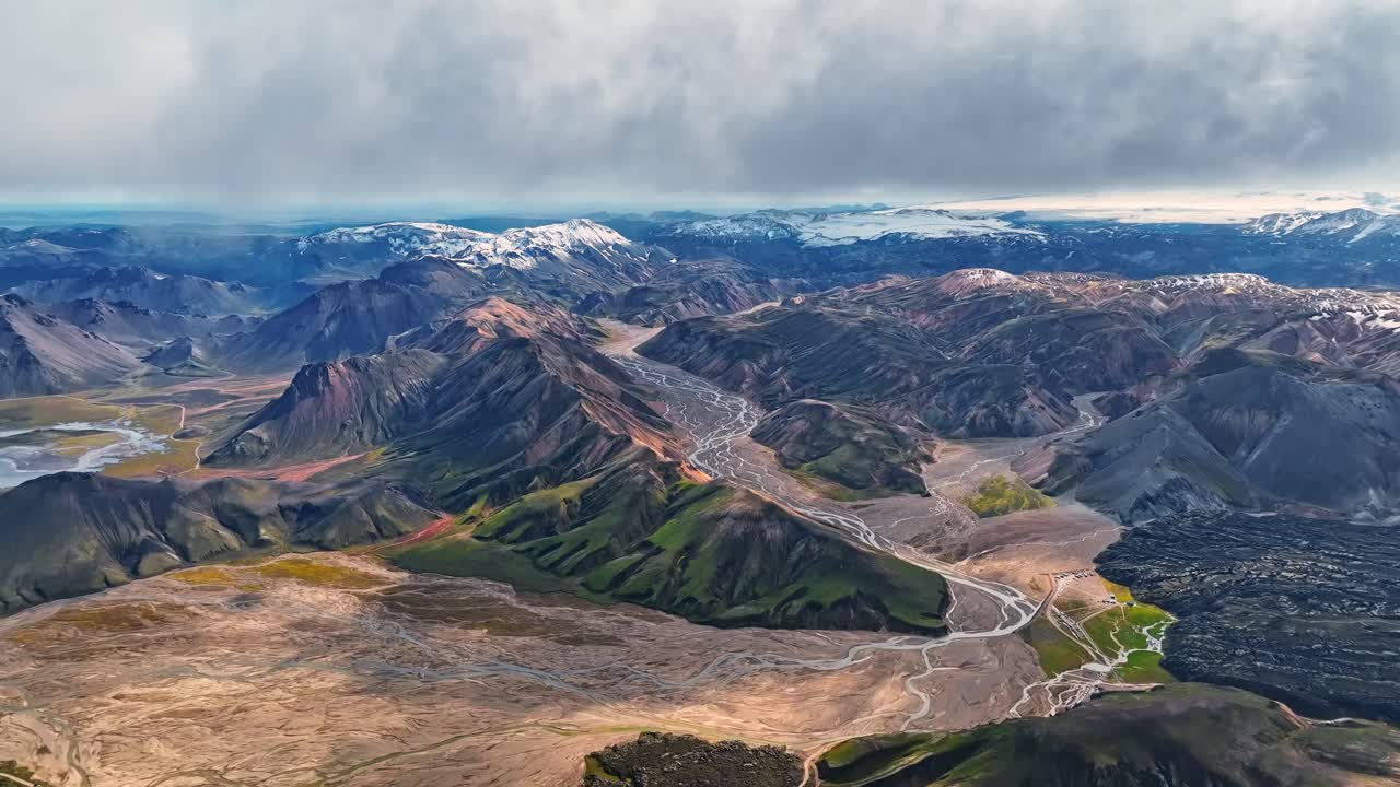 High aerial view of Iceland’s colorful Landmannalaugar mountains with shifting clouds and braided glacial rivers flowing through rugged volcanic terrain