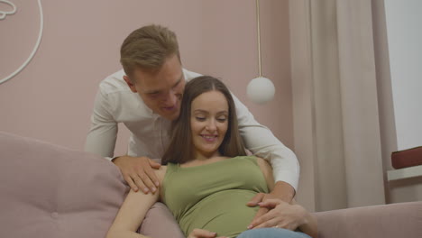 Glückliches-Junges-Schwangeres-Paar,-Das-Sich-Auf-Der-Couch-Umarmt