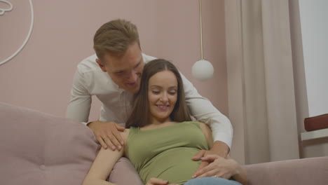 happy young pregnant couple embracing on the couch