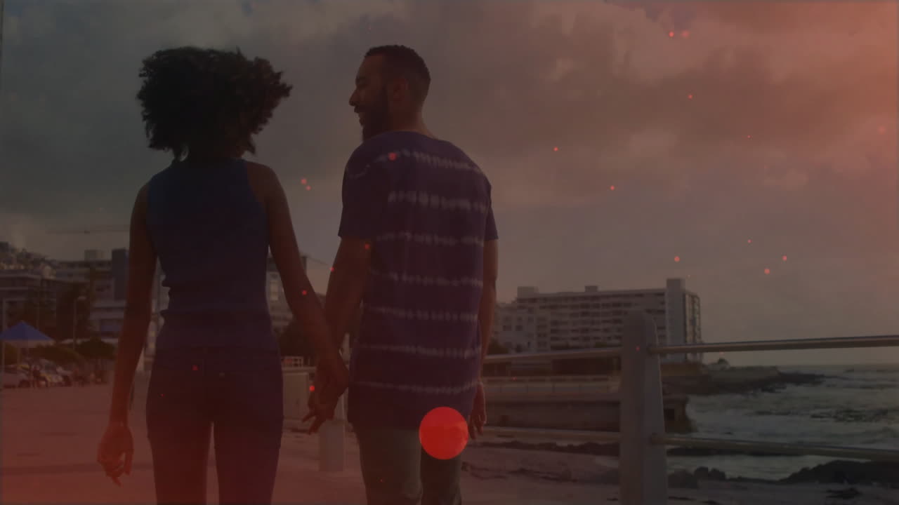 Walking along waterfront, couple holding hands with cityscape in background