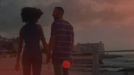 walking along waterfront, couple holding hands with cityscape in background