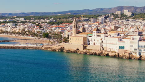 drone captures charming old church surrounded by sailors' town in sunny weather with a beautiful blue sea coast backdrop