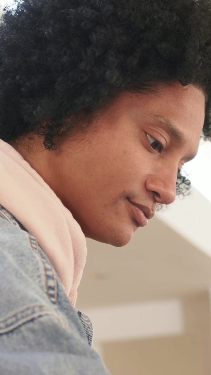 Vertical video: Tilting man checking in lobby as pullback revealing denim jacket, pink hoodie