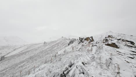 experience the breathtaking beauty of snow-laden mountains and rocky slopes as a drone captures the serene winter landscape at a remote location