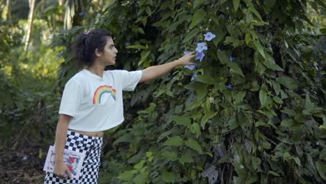 una hermosa niña india con una tapa blanca y un libro en la mano arrancando una flor de la planta