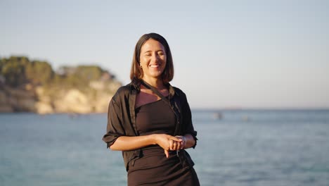 Lächelnde-Kaukasische-Frau-Im-Dunklen-Outfit-Steht-In-Der-Nähe-Der-Strandküste-Von-Mallorca