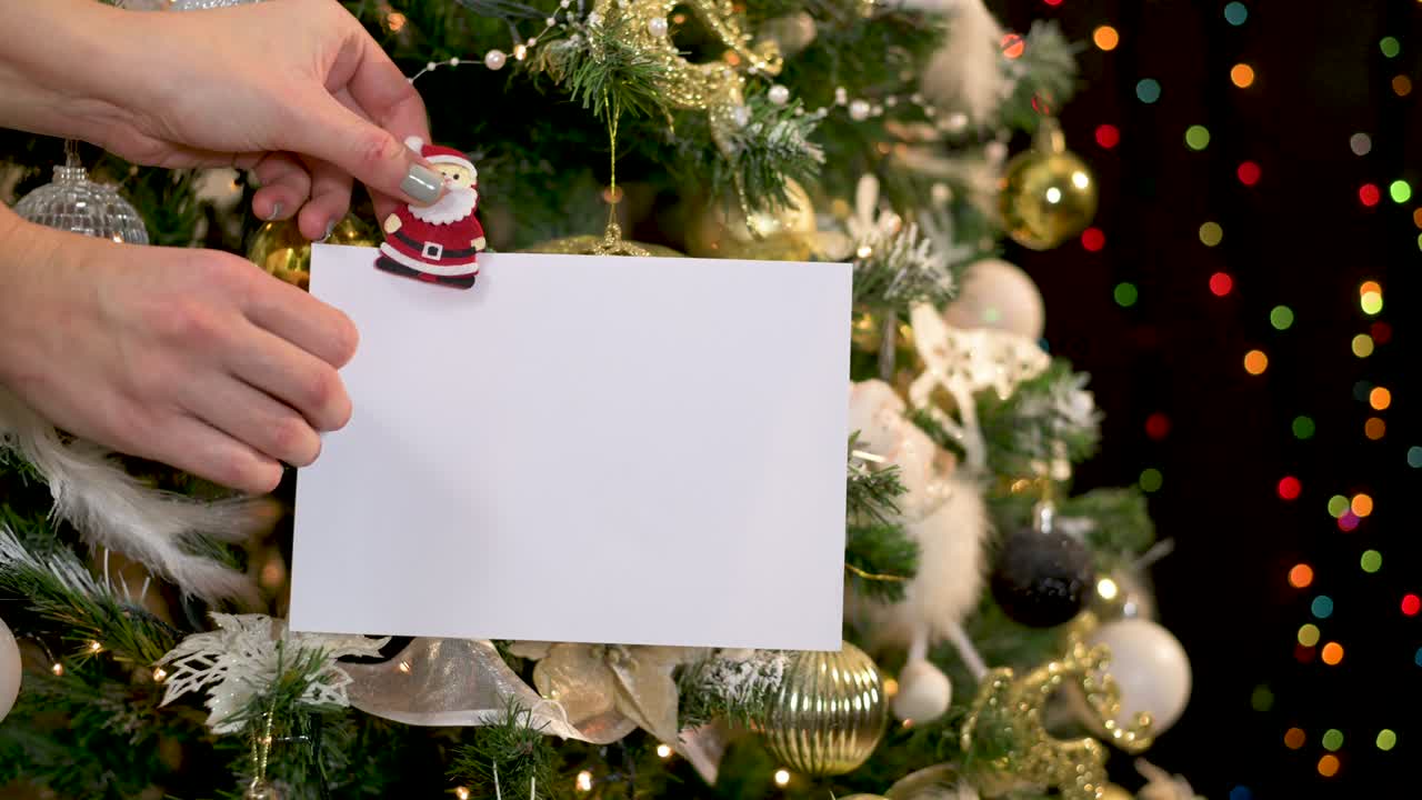 nota de tarjeta de papel enganchado en el árbol de navidad con luces parpadeantes y adornos dorados y blancos