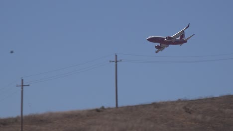 fixed wing aircraft drops fire retardant phos chek on a brush fire burning in the hills of southern california looks like a plane crash behind hillside 1