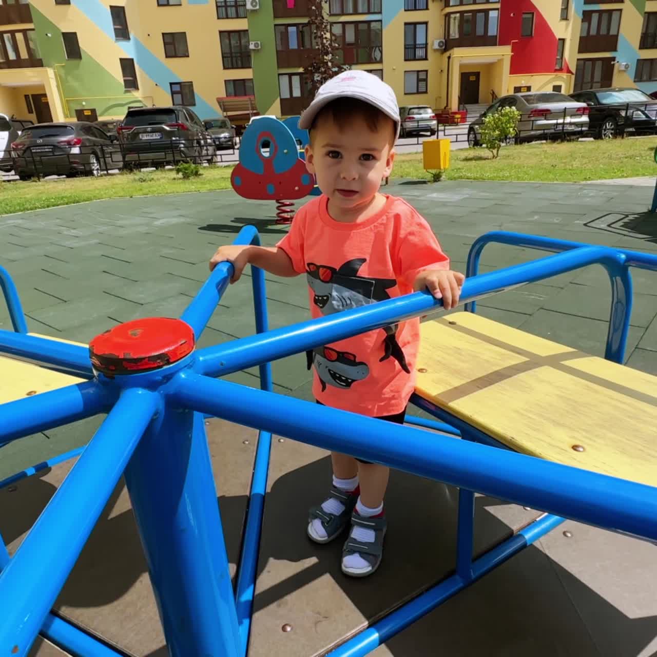 Un niño pequeño de pie en el tiovivo. Un adorable infante en el parque infantil en el patio.