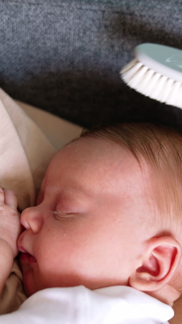 Adorable newborn boy lies comfortably in mom's hands. Dad's hand brushing blond child's hair. Close up. Vertical video