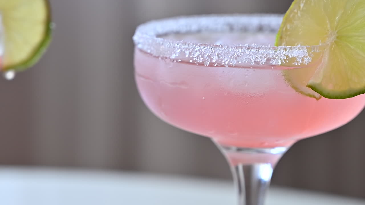 Primer plano de un cóctel rosa claro con hielo y rodajas de lima
