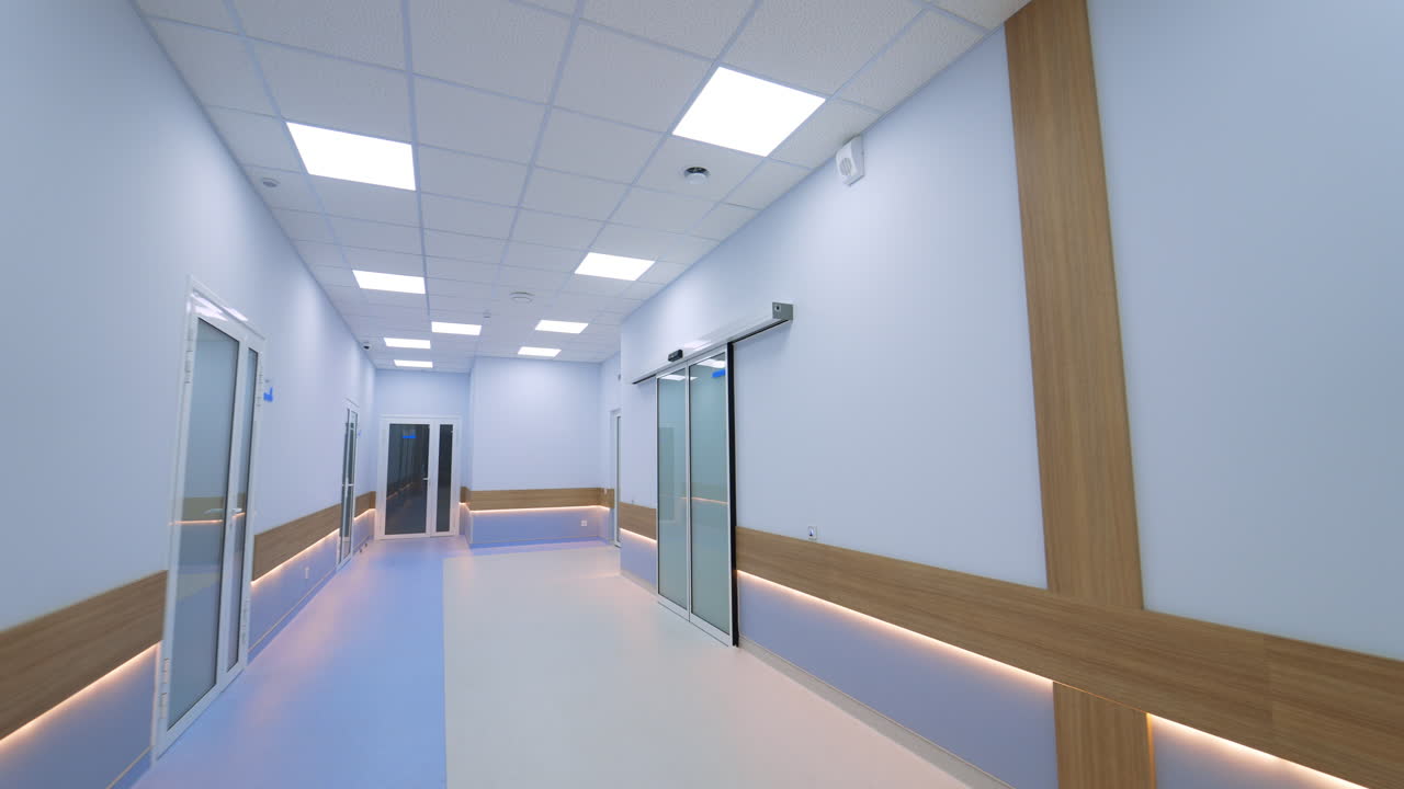 Kyiv, Ukraine, 3 August 2025: Modern hospital hallway with glass sliding doors and LED lighting. Clean clinical corridor with blue walls, wooden panels, and automatic glass doors