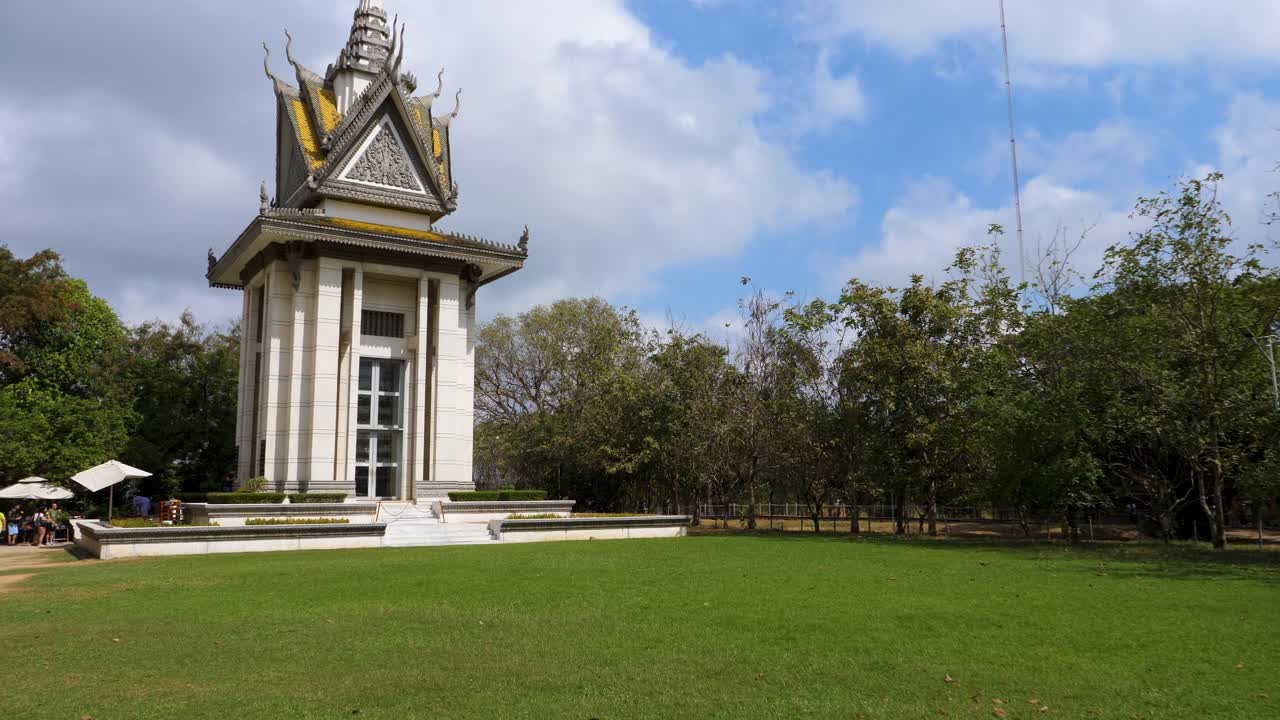 Visitors gather at the Killing Fields memorial in Phnom Penh, reflecting on history and loss under a bright blue sky. The serene atmosphere contrasts the monument's poignant significance