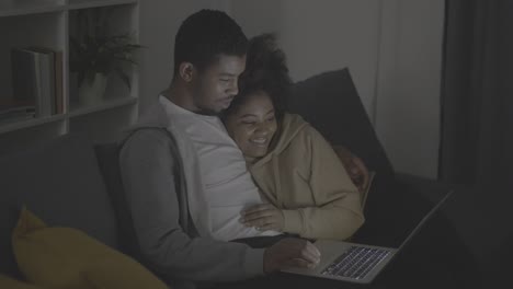 young african american couple laughing while watching a film on the laptop