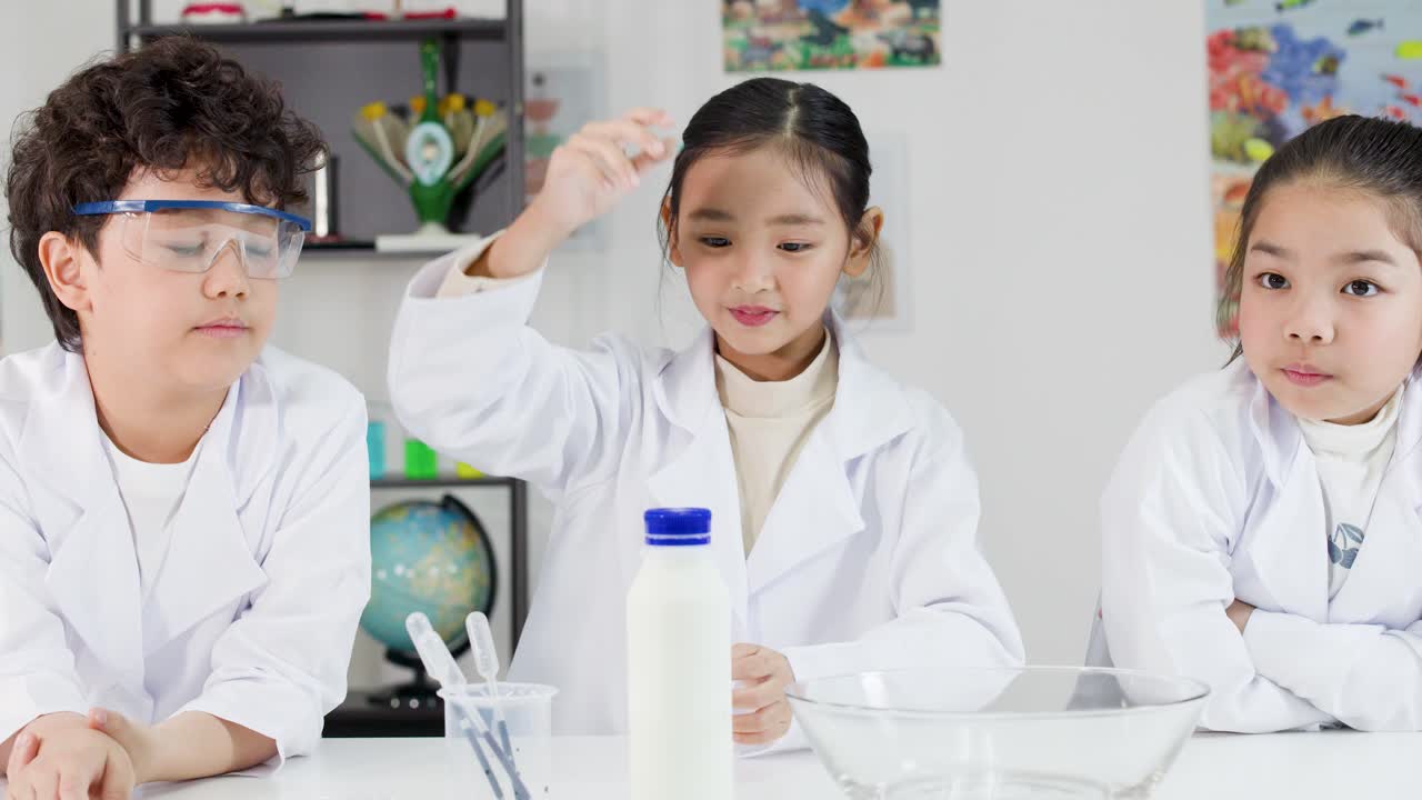 白衣を着た3人の若いアジア人学生が、牛乳と石鹸を使った科学実験を行っている。