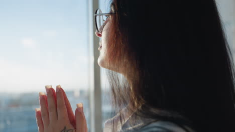 close up of lady calmly pausing with book balanced on head while gazing through building glass wall, bathed in warm sunlight streaming into modern space