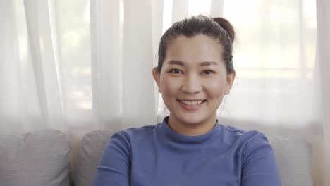 asian woman wearing a blue shirt sitting on a sofa with smiling relax happily